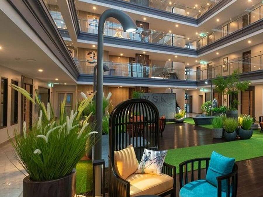 Un atrium à plusieurs niveaux, doté d’un espace de détente central avec une table ronde et des chaises, entouré de plantes en pot et d’une structure métallique décorative.