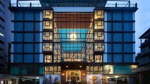 A modern hotel with a central glass facade, multiple floors, and a prominent entrance with steps. - VSK RESIDENCE At Suvarnabhumi Airport (Bang Phli)