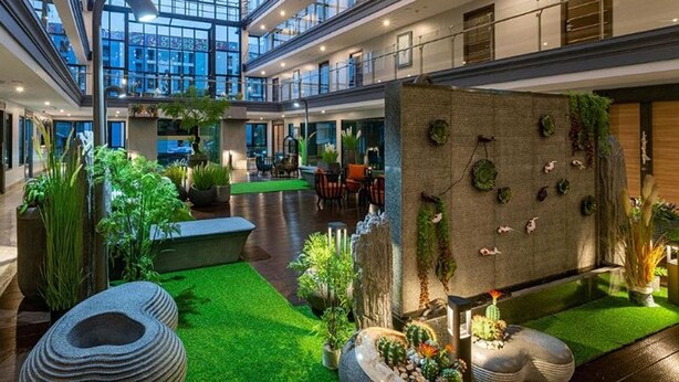 A spacious atrium with a central seating area, surrounded by indoor plants and a water feature. - VSK RESIDENCE At Suvarnabhumi Airport (Bang Phli)