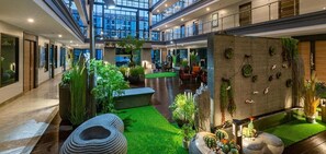 A spacious atrium with a central seating area, surrounded by indoor plants and a water feature. - VSK RESIDENCE At Suvarnabhumi Airport (Bang Phli)