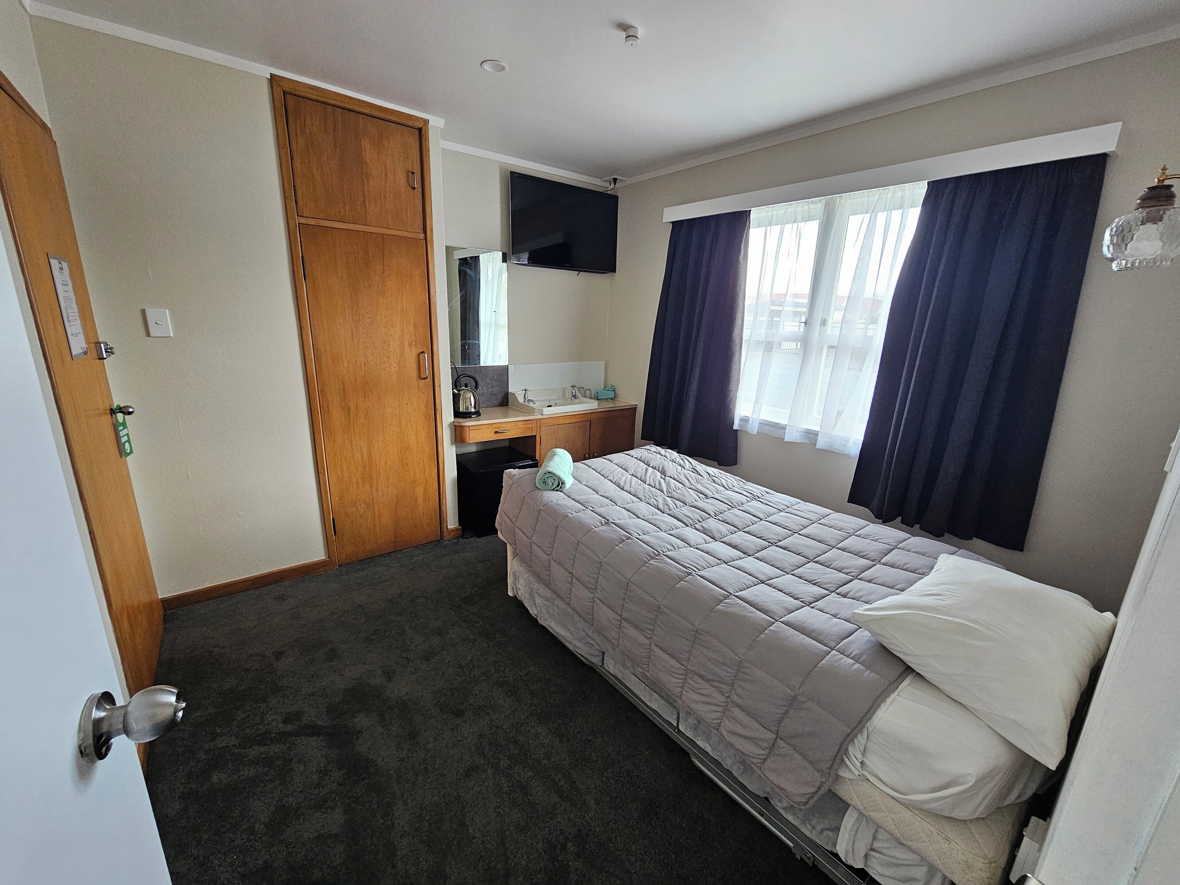 Une chambre d’hôtel comprenant un lit, un bureau avec un ordinateur, une armoire et un téléviseur.