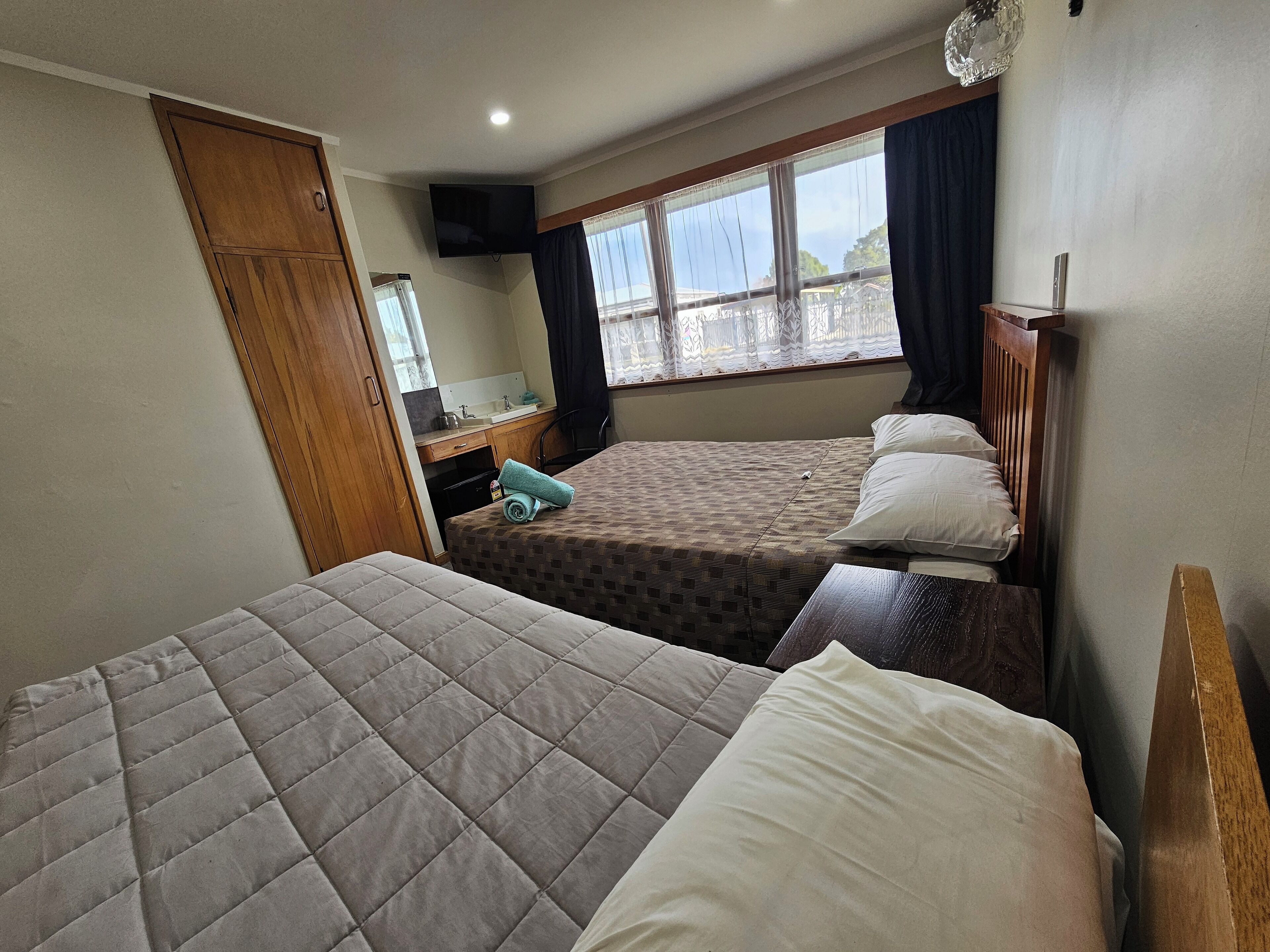 Habitación de hotel con dos camas, un armario de madera, un escritorio pequeño con espejo y una ventana con cortinas.