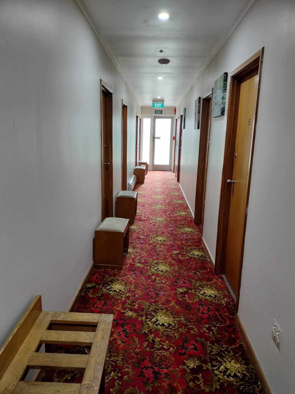 A hotel hallway with carpeted floors, wooden doors, and a bench.