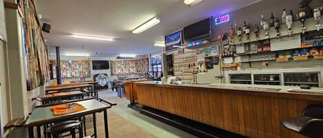 Un espace bar doté d’un comptoir en bois, de tabourets de bar et d’un téléviseur fixé au-dessus du bar.