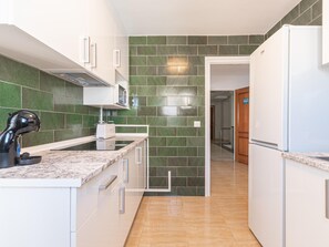 A modern kitchen with green tiles, white cabinets, a built-in microwave, and a toaster.