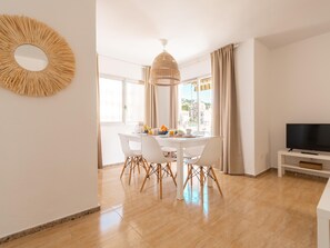 A modern dining area with a white table and chairs, a hanging light fixture, and a television on a stand.