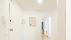 Ein Flur mit einer weißen Tür, einem Telefon, einem kleinen Gemälde und einem Spiegel an der Wand.