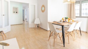 Ein heller, geräumiger Raum mit einem Holzespeisetisch, der für ein Frühstück gedeckt ist, weißen Stühlen und einer hängenden Leuchte.