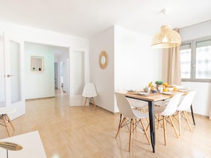A bright, spacious room with a wooden dining table set for breakfast, white chairs, and a hanging light fixture. - Primera linea New Borodin AB Family Apart. 5º1ª (Lloret de Mar)