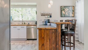 Une cuisine avec des meubles blancs, un îlot central en bois et un panneau indiquant l’emplacement du café.