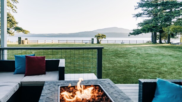 Une terrasse agrémentée d’un foyer extérieur, de coins salon et offrant une vue sur un lac et des montagnes.