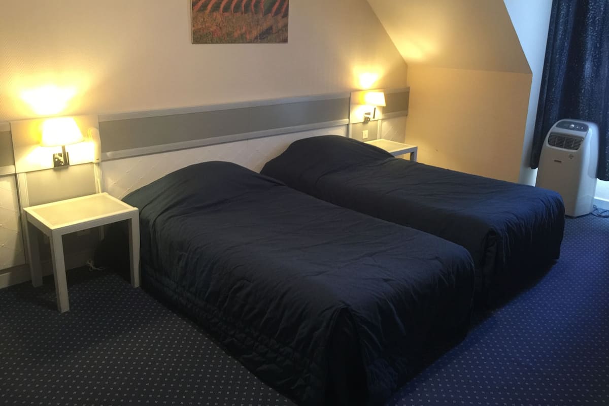 Ett hotellrum med två sängar, ett nattduksbord, en lampa, en värmare och en tavla på väggen.