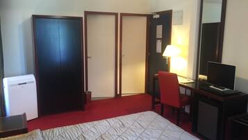 A hotel room with a bed, a desk with a chair, a television, a desk lamp, and a refrigerator.