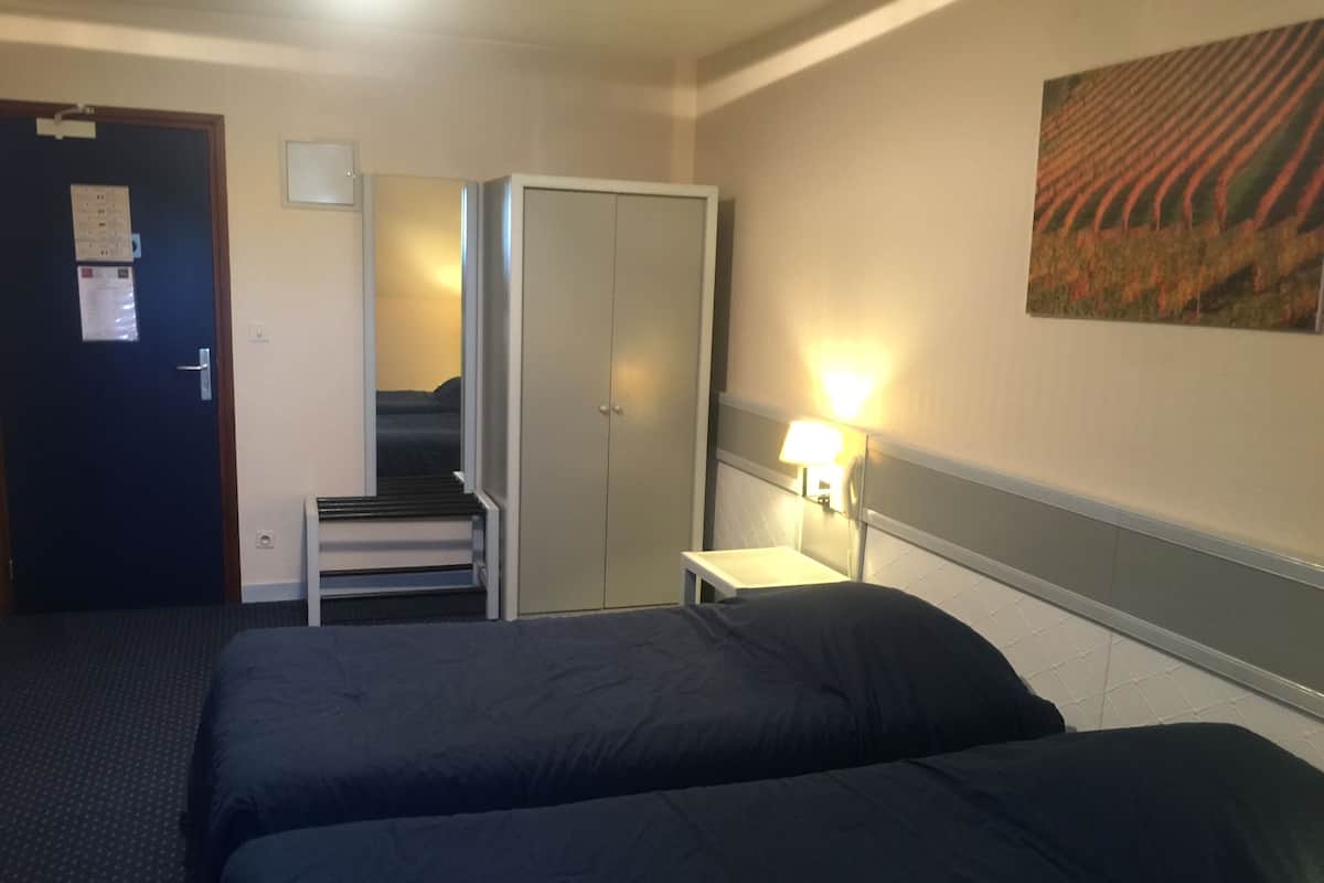 Ett hotellrum med två sängar, ett skrivbord, en stol, en garderob, en dörr och en vägglampa.