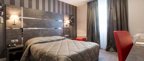 A hotel room with a bed, a red chair, a nightstand, a lamp, and a wall with a textured design.