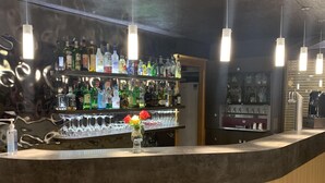 A bar area with a curved counter, shelves of liquor bottles, and hanging pendant lights. - Hostellerie Saint-Vincent (Nuits-Saint-Georges)