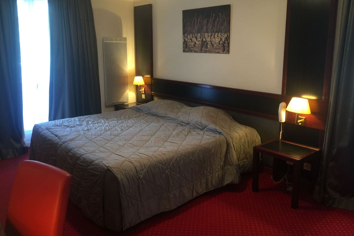 Ett hotellrum med en stor säng, två sänglampor, ett nattduksbord, en stol och en tavla på väggen.