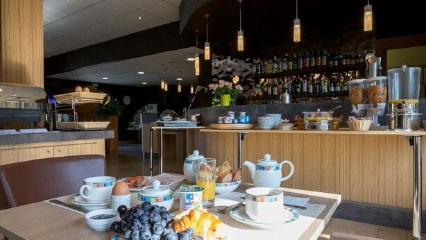 A breakfast setup with a table, breakfast items, and a bar area in the background. - Hostellerie Saint-Vincent (Nuits-Saint-Georges)