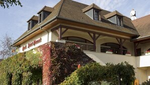 A hotel with a covered outdoor area, a balcony with flowers, and a large window. - Hostellerie Saint-Vincent (Nuits-Saint-Georges)