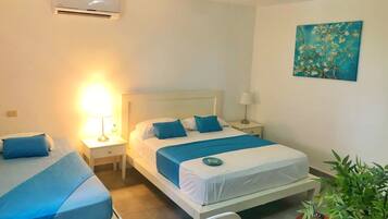 A hotel room with two beds, a nightstand with a lamp, an air conditioner, a painting on the wall, and a potted plant.
