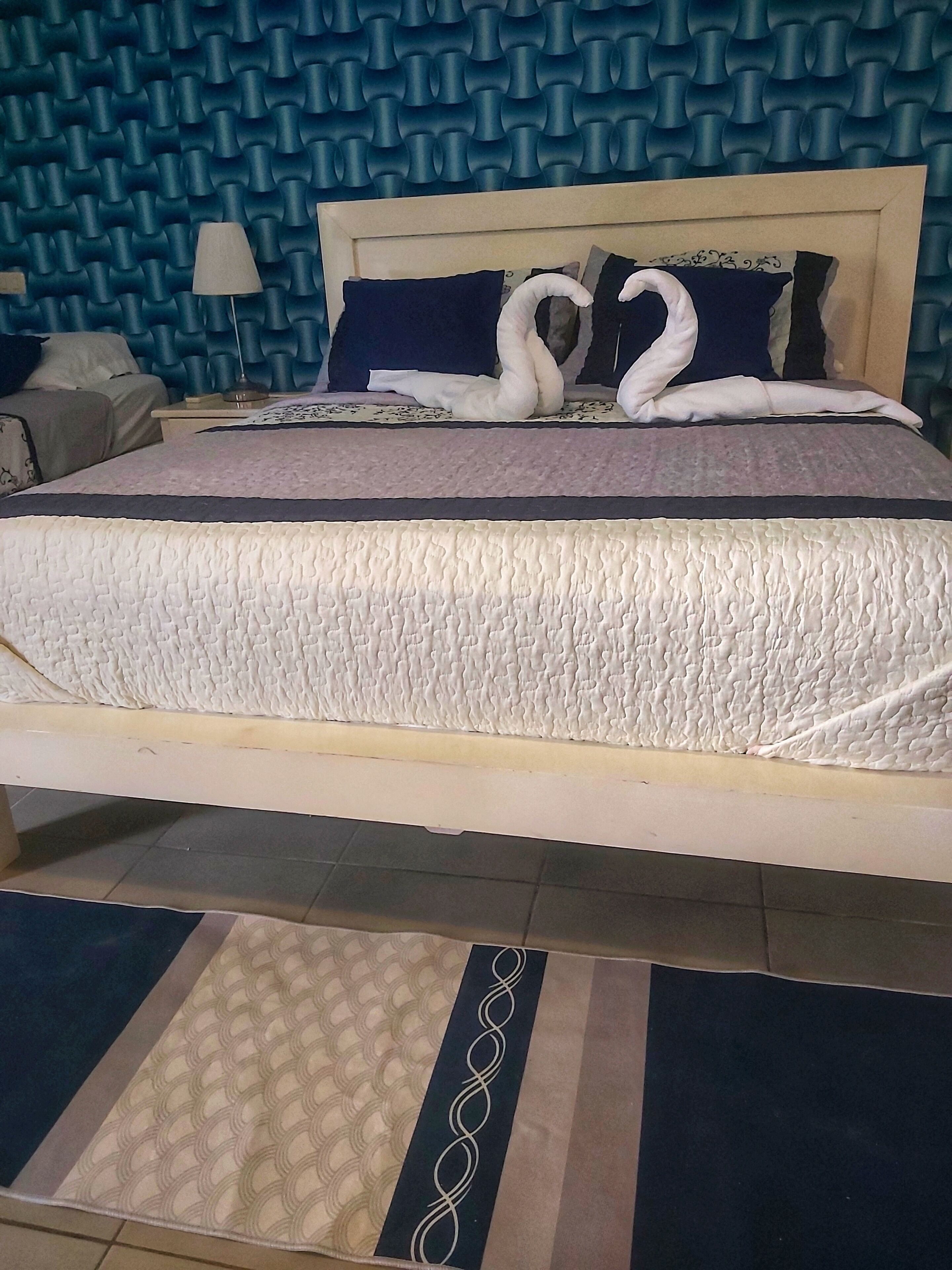 A neatly made bed with a patterned bedspread, pillows, and a decorative swan design on the pillows.