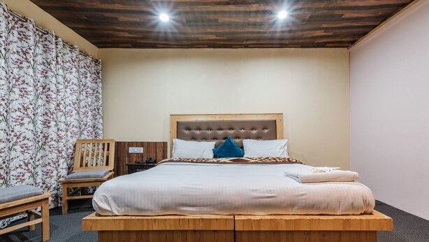 Un dormitorio con cama de madera, una silla, una mesita de noche y una cortina con motivos florales.