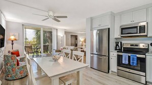 A modern kitchen with stainless steel appliances, a dining area with a white table, and a balcony with outdoor seating. - 2 QUEEN BEDS | FREE WIFI |  HEATED POOLS | FREE PARKING | STEPS TO BONITA BEACH (Bonita Springs)