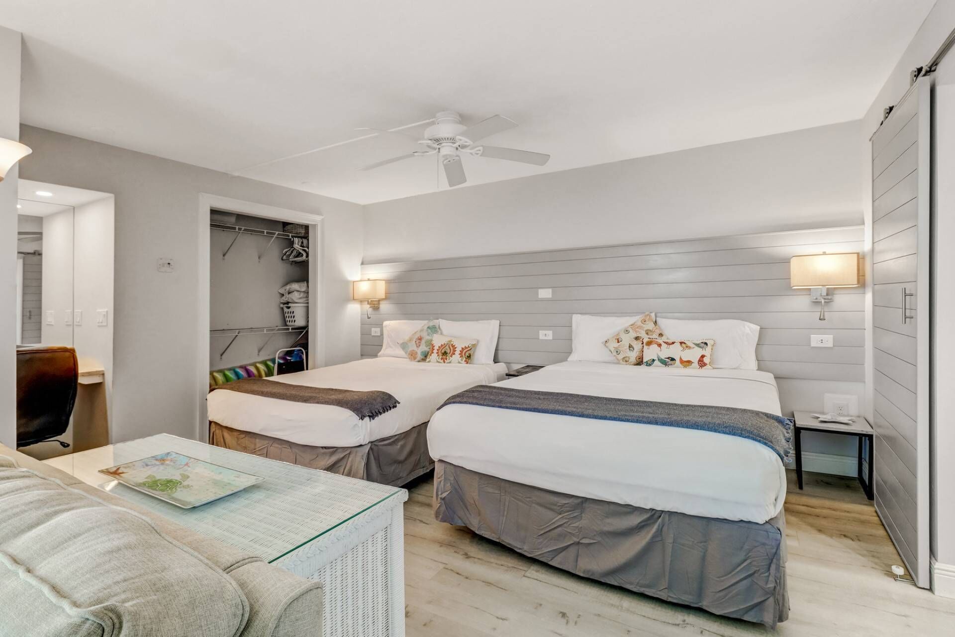 A modern bedroom with two beds, a ceiling fan, and a bedside table with a lamp.