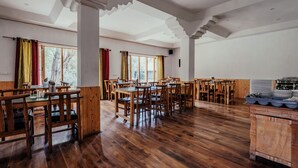 Un comedor amplio con mesas y sillas de madera, ventanas grandes con cortinas y una mesa de buffet.