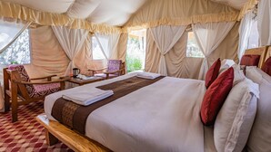 Una habitación tipo tienda de campaña con una cama, una silla, una mesa y cortinas.
