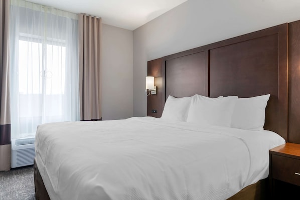 Habitación de hotel con una cama grande, una mesita de noche, una lámpara de pared y una ventana con cortinas.