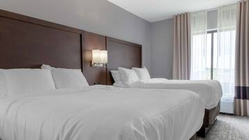 A hotel room with two beds, a large window with curtains, and a wall-mounted light fixture.