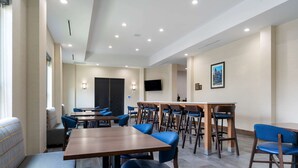 A modern hotel dining area with multiple tables and chairs, a flat-screen TV, and a large window providing natural light. - Comfort Suites Paducah Mall Area (Paducah)