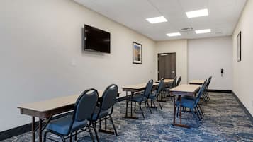 A conference room with tables and chairs, a flat-screen TV, and a door.