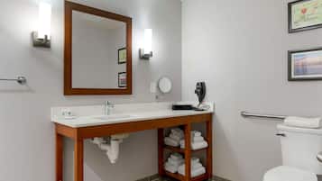 A bathroom with a wooden vanity, a mirror, a toilet, and a shelf with towels.