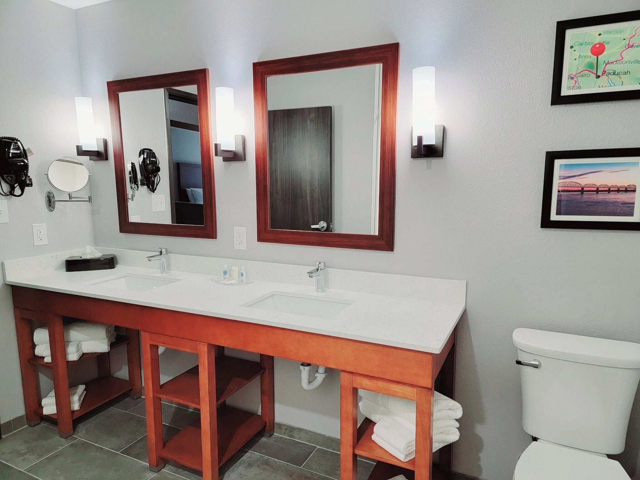 A bathroom with a double sink vanity, two mirrors, a toilet, and a framed map on the wall.