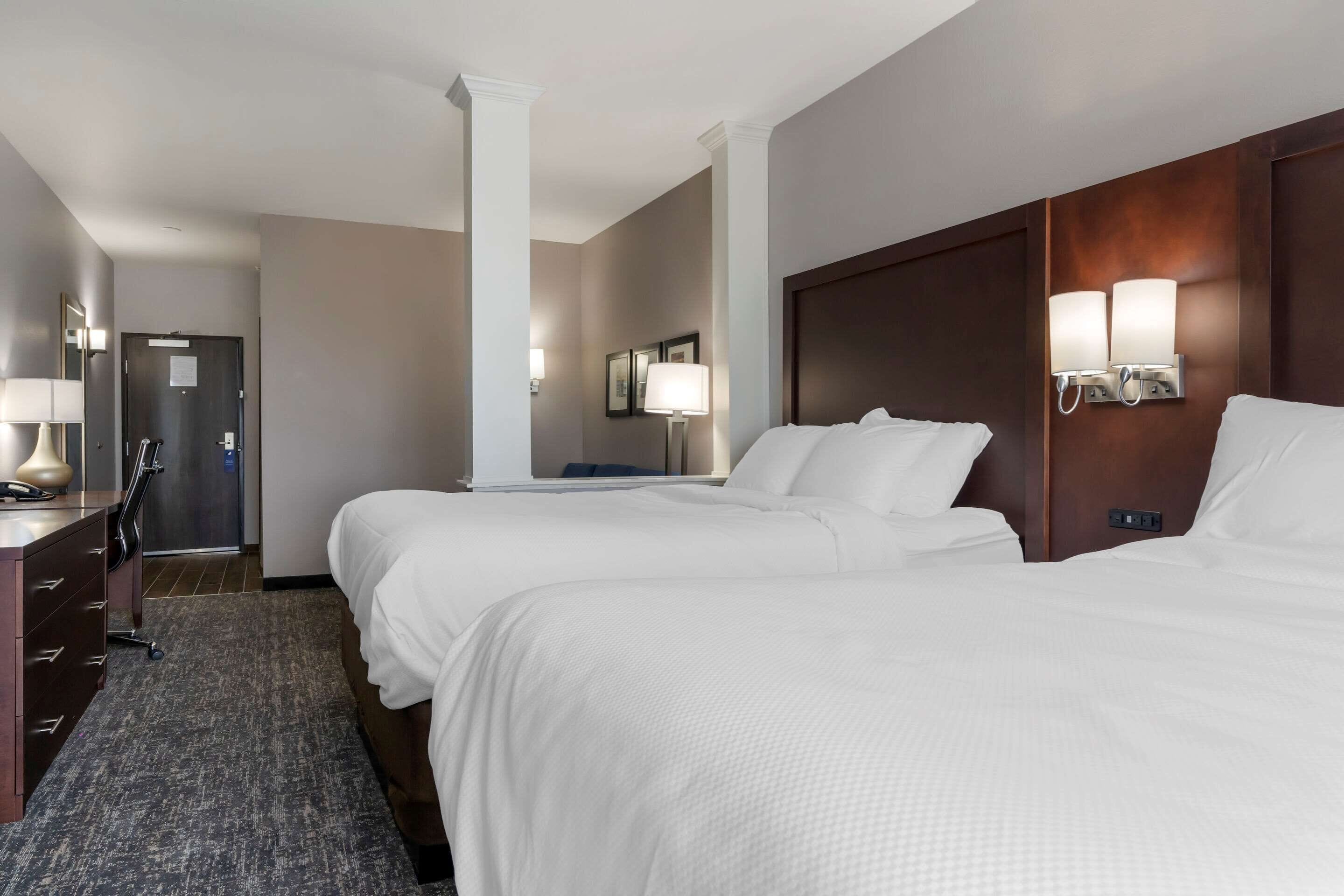Una habitación de hotel con dos camas, un escritorio con lámpara y una puerta.