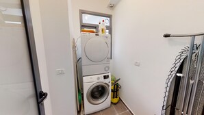 Een kleine wasruimte met een voorlader wasmachine, een gestapelde droger en een klein raam boven de droger.