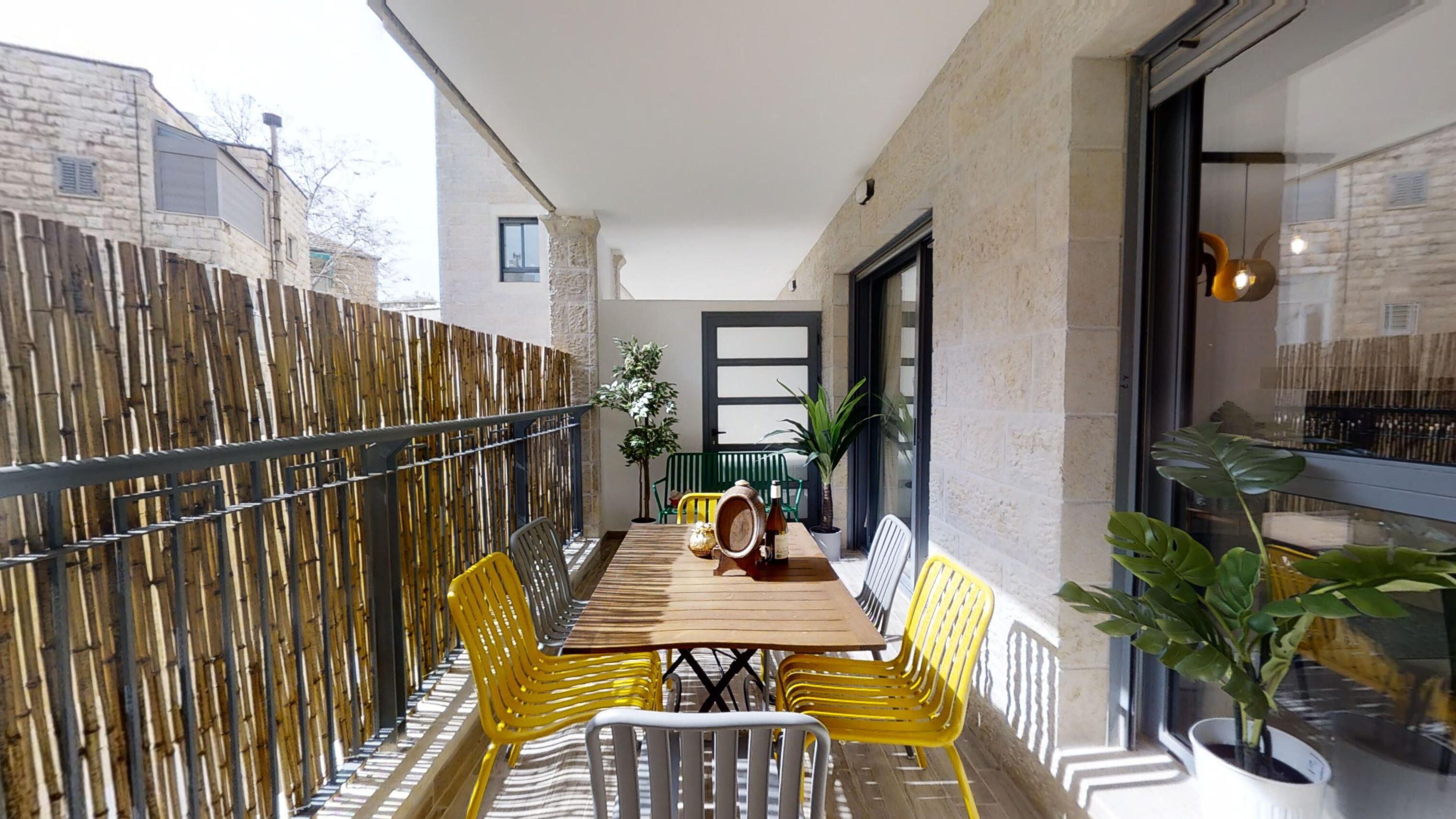 Ein Balkon mit Holztisch, gelben Stühlen und Topfpflanzen.