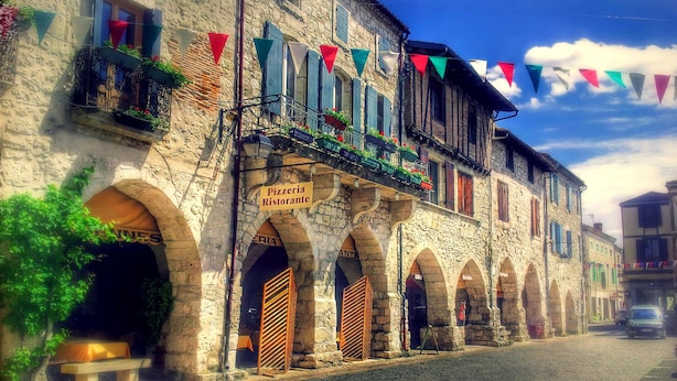 Ein historisches Steinhaus mit einem Pizzaria-Schild, Bogenportalen und einer Kopfsteinpflasterstraße.