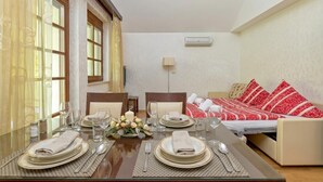 A dining area with a table set for four, a sofa bed with red and white bedding, and a wall-mounted air conditioner. - Pool Villa Silva Marija (Brezice)