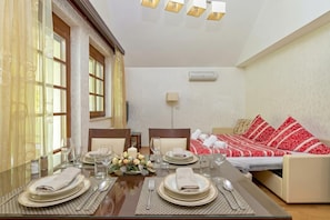 A dining area with a table set for four, a sofa bed with red and white bedding, and a wall-mounted air conditioner. - Pool Villa Silva Marija (Brezice)