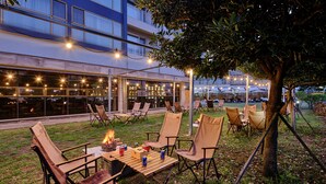 An outdoor seating area with tables and chairs, a fire pit, and string lights.