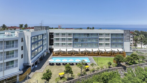 A modern hotel with a rooftop pool, multiple balconies, and a view of the sea.