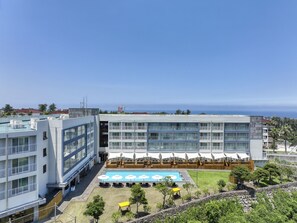 Un hotel moderno con piscina en la azotea, varios balcones y vistas al mar.