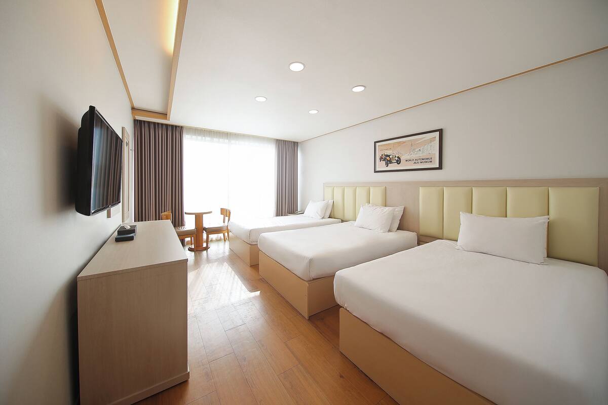 A hotel room with two beds, a desk, a chair, and a television.