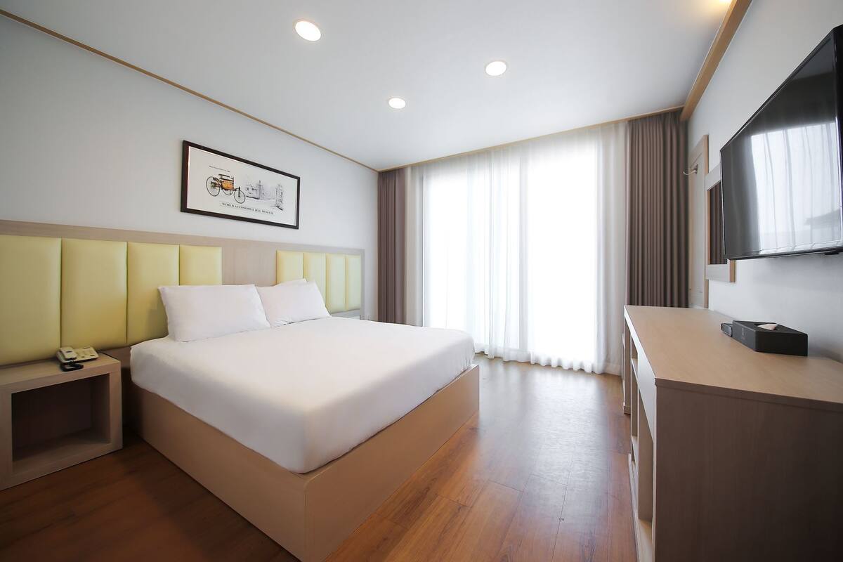 A hotel room with a large bed, bedside table, and a desk with a flat-screen TV.