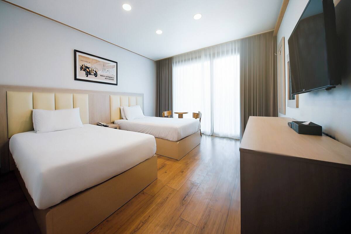 A hotel room with two beds, a flat-screen TV, a desk, and a framed picture on the wall.