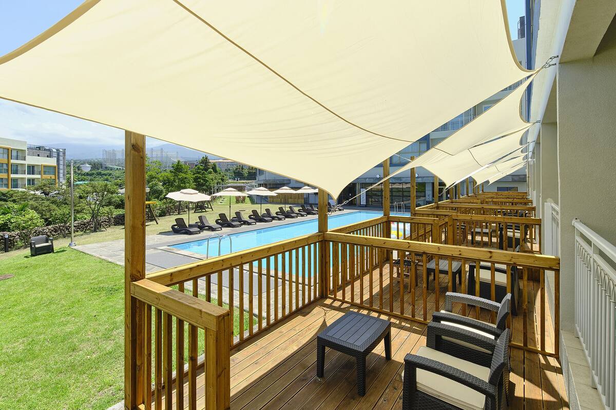A wooden deck with a pool, lounge chairs, and umbrellas.