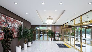 A hotel lobby with a marble floor, a chandelier, potted plants, and glass doors leading to the hotel rooms.